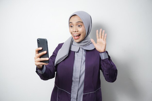 Cheerful beautiful Asian woman in casual shirt and hijab using a mobile phone isolated by white background