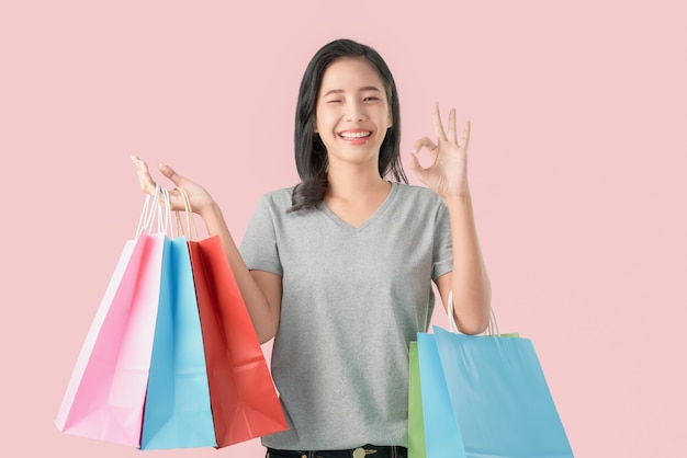 Cheerful beautiful Asian woman holding multi coloured shopping bags and shows ok sign