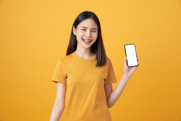 Cheerful beautiful Asian woman holding smartphone on light yellow wall