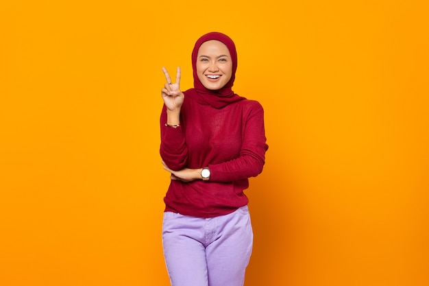 Cheerful beautiful girl in red sweater posing in front of camera showing peace sign with two hands