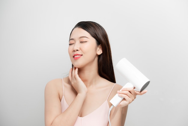 Cheerful beautiful girl in towel smiling laughing singing with hair dryer making funny face over white background. Beauty spa and cosmetology.