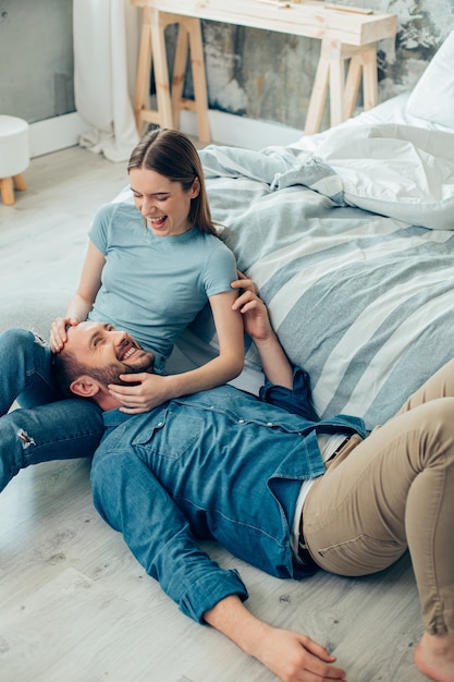 Cheerful beautiful lady sitting on the floor and smiling to her beloved man lying on her legs