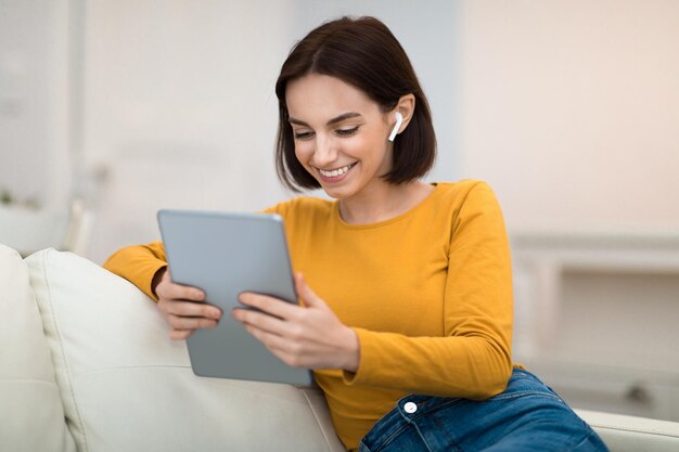 Cheerful beautiful lady using digital pad and earpods at home