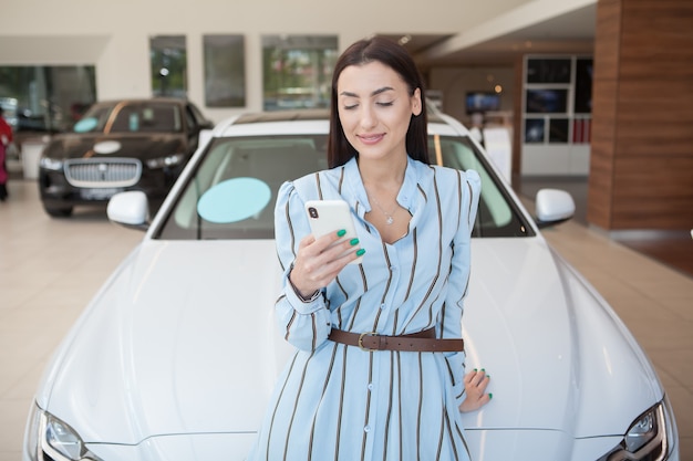 Cheerful beautiful woman using smart phone at the dealership