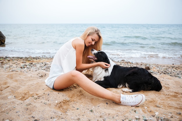 ビーチで彼女の犬を抱き締める陽気な美しい若い女性