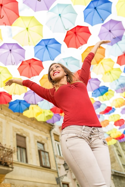 Фото Веселая красивая молодая женщина на улице украшена множеством разноцветных зонтиков.