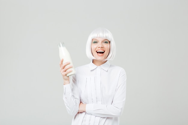 Bella giovane donna allegra che ride e che tiene bottiglia di latte