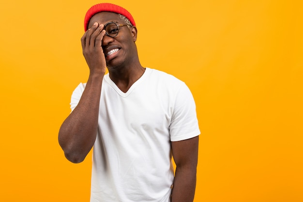 Cheerful black american man in white t-shirt smiling covering his face with his hand on yellow with copy space