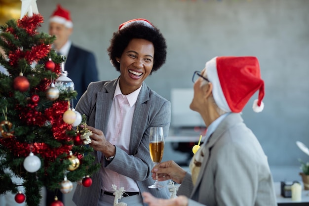 Cheerful black businesswoman and her colleague having fun while decorating Christmas tree in the office