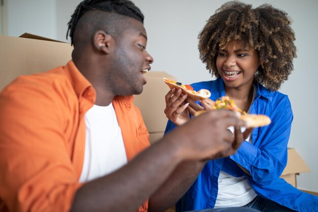 ピザを食べて、引っ越しの日に楽しんでいる陽気な黒人カップル