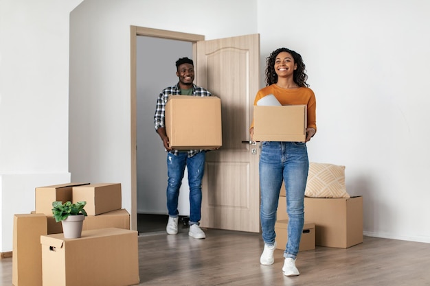 Cheerful Black Couple Entering New House Carrying Moving Boxes Indoor