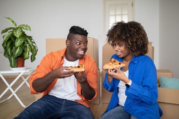 Cheerful black couple having pizza lunch break after moving into new home