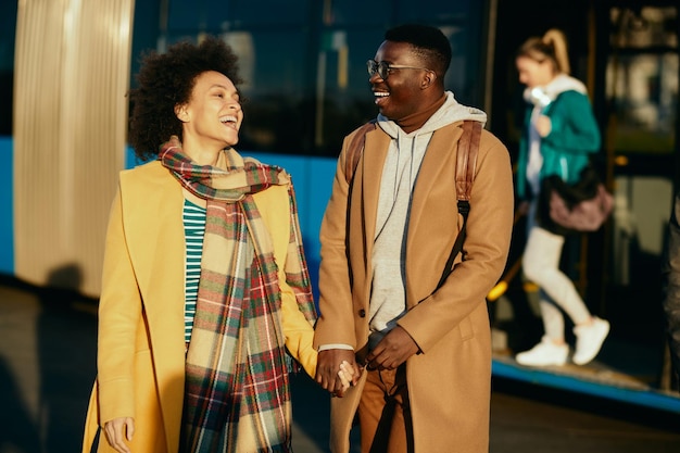 Cheerful black couple holding hands and having fun at bus station