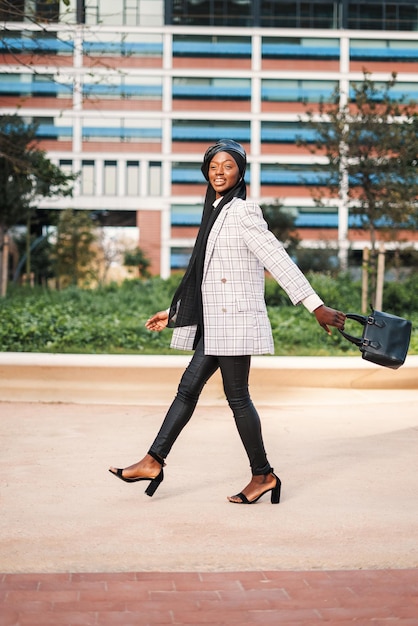 Cheerful black lady in stylish wear walking in city park