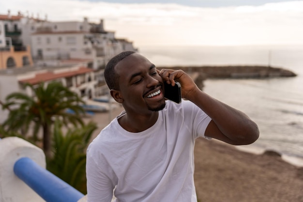 Cheerful black man talking on cellphone at beach