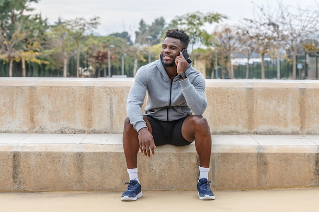 Веселый чернокожий спортсмен разговаривает по смартфону.