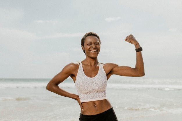 Cheerful black woman flexing her muscles by the seaside