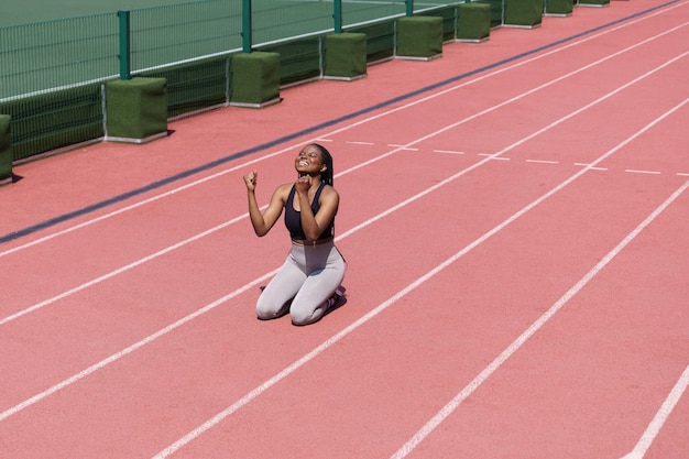 Cheerful black woman wins after running long distance on\
terracotta track of modern sports complex