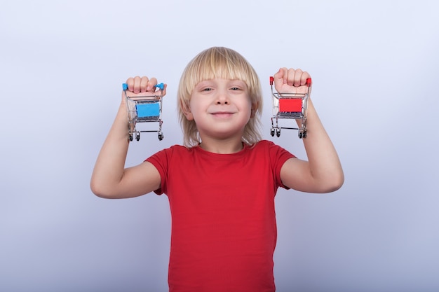 Ragazzo biondo allegro che tiene in mano due piccoli carretti della drogheria