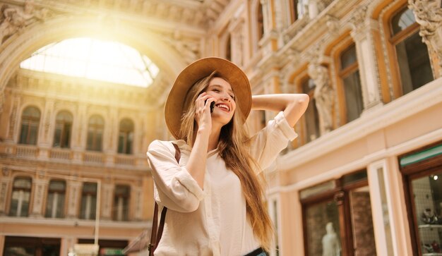 Cheerful blond woman in felt hat talking on the phone the old urban architecture