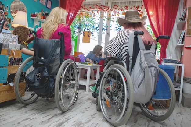 Cheerful blond woman her friend in a hat in a wheelchair public library.