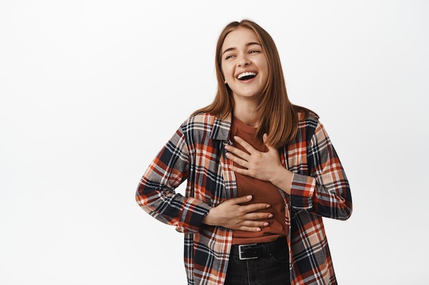 Photo cheerful blond woman smiling, laughing and looking aside at smth funny, chuckle from joke, having fun, standing in casual clothes against white wall