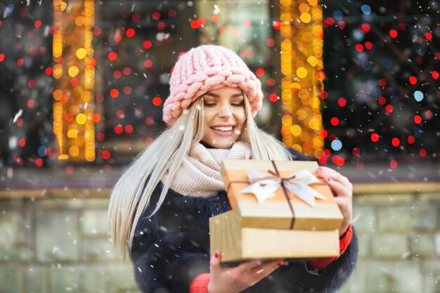 Cheerful blond woman wears knitted pink hat enjoying gift at the winter fair