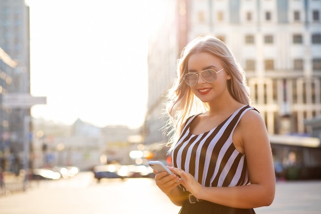 Cheerful blonde girl holding mobile phone typing message. Space for text