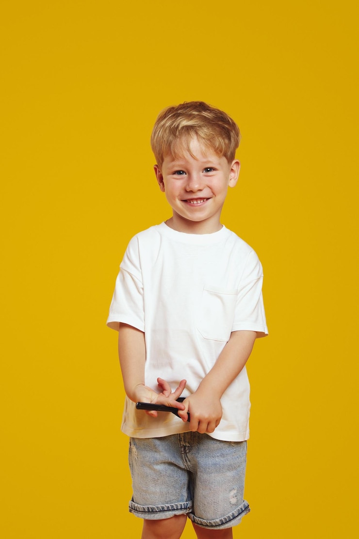 Photo 白いtシャツを着た陽気な金 ⁇ の子供が黄色い背景に立って微笑んでいる