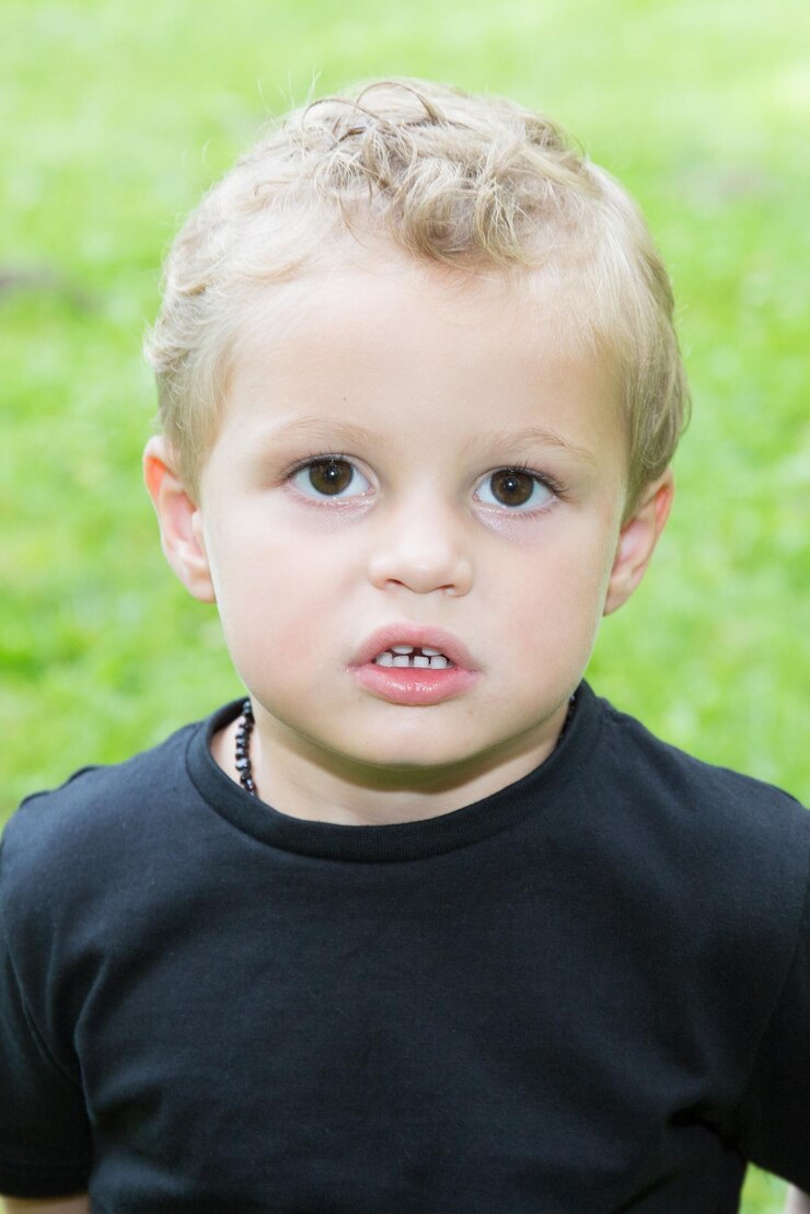Cheerful blonde little boy outdoors on the grass Child face close up