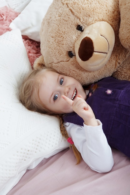 Cheerful blonde little girl lies on big soft toy bear