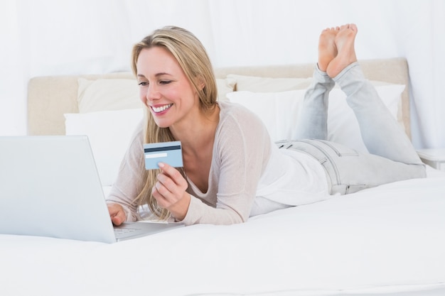 Веселая блондинка, покупающая онлайн на кровати