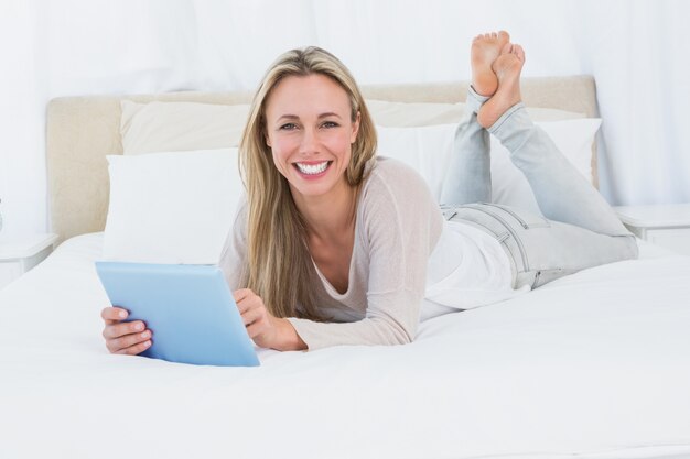 Cheerful blonde using tablet pc on the bed