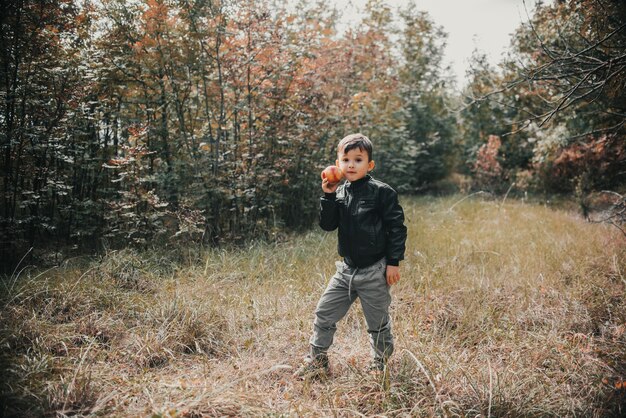 A cheerful boy in the autumn forest with an apple in his hands