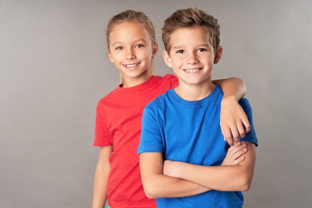 Cheerful boy and girl standing against gray background