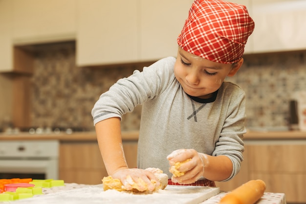 Веселый мальчик веселится во время приготовления теста для печенья