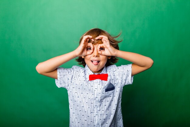 Cheerful boy holding hands near face in form of mask isolated on green background