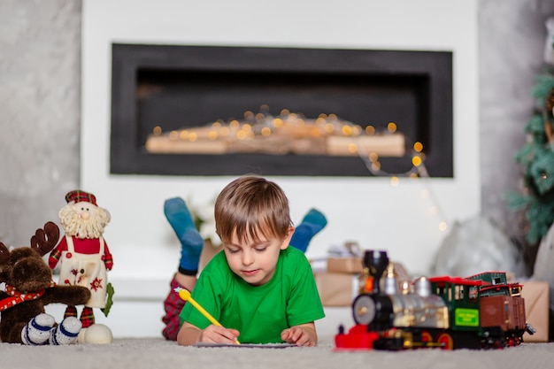 Cheerful boy is a letter to Santa, near the Christmas tree. Happy childhood, time for fulfilling wishes.