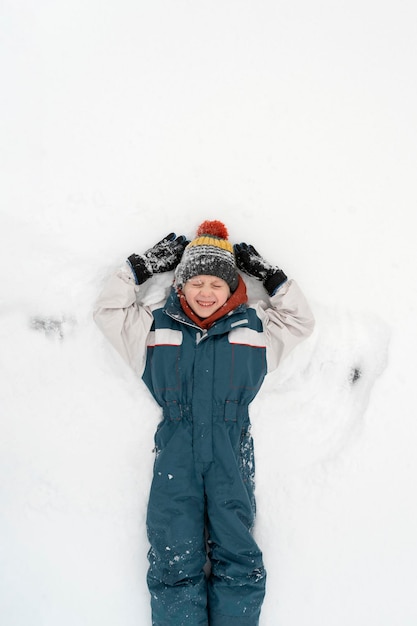 元気な男の子が雪の中に横たわり、スノーエンジェルを作ります。幸せな子供時代。上面図。