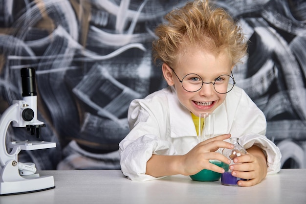 Cheerful boy looks closely at the reaction in flasks after mixing substances