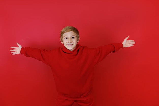 Cheerful boy on a red background and dressed in a red suit stretched out his arms to the sides