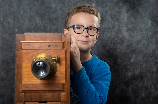 Фотограф жизнерадостного мальчика ретро с винтажной деревянной камерой