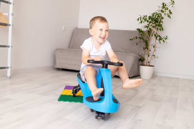 A cheerful boy rides a blue car at home in the living room