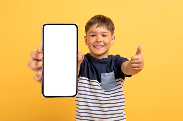 Cheerful boy showing smartphone with white screen thumb up