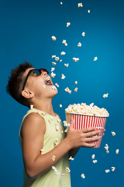 Cheerful boy with a bucket of popcorn, a lot of popcorn falls from above, the boy catches him, fun and entertainment, the concept of rest