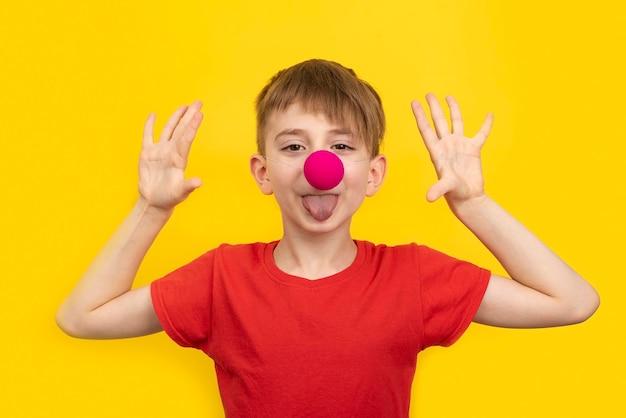 Cheerful boy with red clown nose and red tshirt on yellow background 1 April Fools day concept