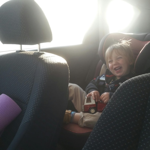 Фото Веселый мальчик с игрушкой сидит в машине в солнечный день