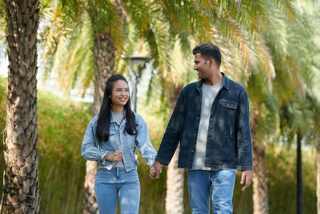 Cheerful boyfriend and girlfriend holding hands and looking at each other when walkingin park