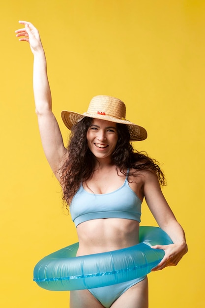 cheerful brunette girl in blue swimsuit with inflatable swimming circle dances on yellow background