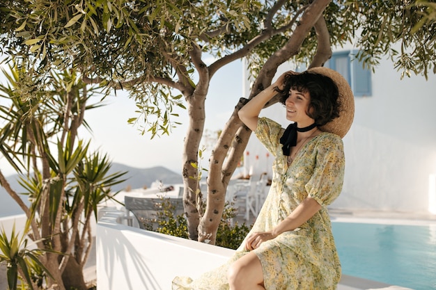 Cheerful brunette lady in floral dress holds boater